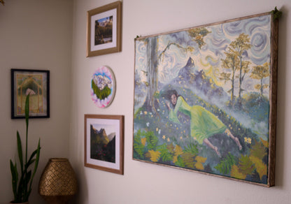 A large framed art print depicting a woman in a green dress in a forest landscape with swirling blue and yellow sky, displayed on a beige wall alongside other framed art pieces.
Arwen's Sorrow, Original Oil Painting with Custom Frame - Inspired by Lord of the Rings. Painting by Kelsey Weirick